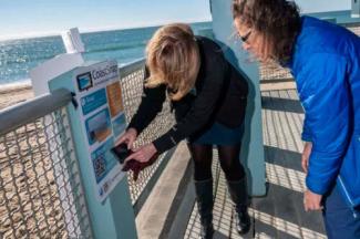 Ogren and Rubinoff scan the QR code on the CoastSnap cradle, which community photographers can use to submit a photo that will help government agencies monitor the changing coastline. 