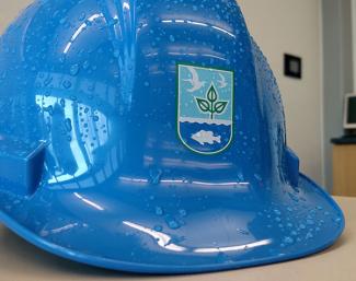 Blue hard hat with Rhode Island DEM logo sits in an office with water droplets on it 
