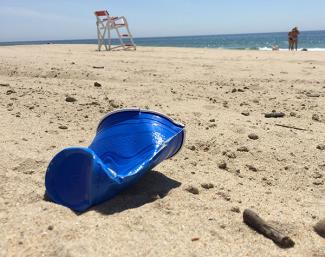 A crushed plastic cup lies in the sand next to a discarded cigar with a lifeguard chair and waves in the background atMisquamicut State Beach in Westerly