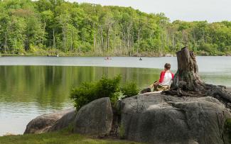 Park visitor sitting atop a large rock overlooking Olney Pond at Lincoln Woods State Park