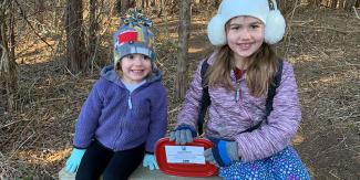 Two children smile in a forested area after successfully finding a letterbox