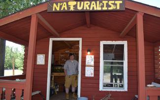 A park naturalist stands in the doorway to a cabin with a handpainted sign that reads, "Naturalist"