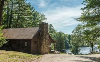 A historic cabin sits overlooking the blue waters of Peck Pond