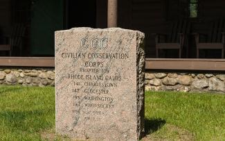 A chisled granite plaque with the words, "CCC. Civilian Conservation Corps, Chapter 109. RHode Island Camps: 141 Charlestown, 142 Glocester, 195 Washington, 1161 Woonsocket, 1186 Escoheag, 1186 Greene, 1188 Hope"
