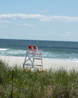 A sandy white beach with blue ocean waves with a lifeguard chair in the distance anddune grass in the foreground
