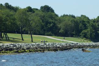 Shoreline of Colt State Park with grassy fields and paved walking path along the blue waters of Narragansett Bay
