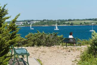 A person sits on a bench overlooking sailboats in Narragansett Bay at Fort Wetherill State Park