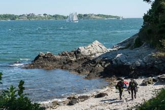 Two scuba divers in full gear walk along the rocky beach at Fort Wetherill State Park