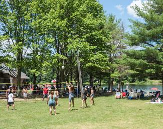 A large group playing volleyball while others relax in the shade near Olney Pond beach pavilion at Lincoln Woods State Park
