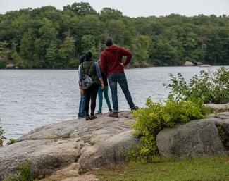 A group of hikers dressed for cold weather stand on a rock overlooking Olney Pond at Lincoln Woods State Park
